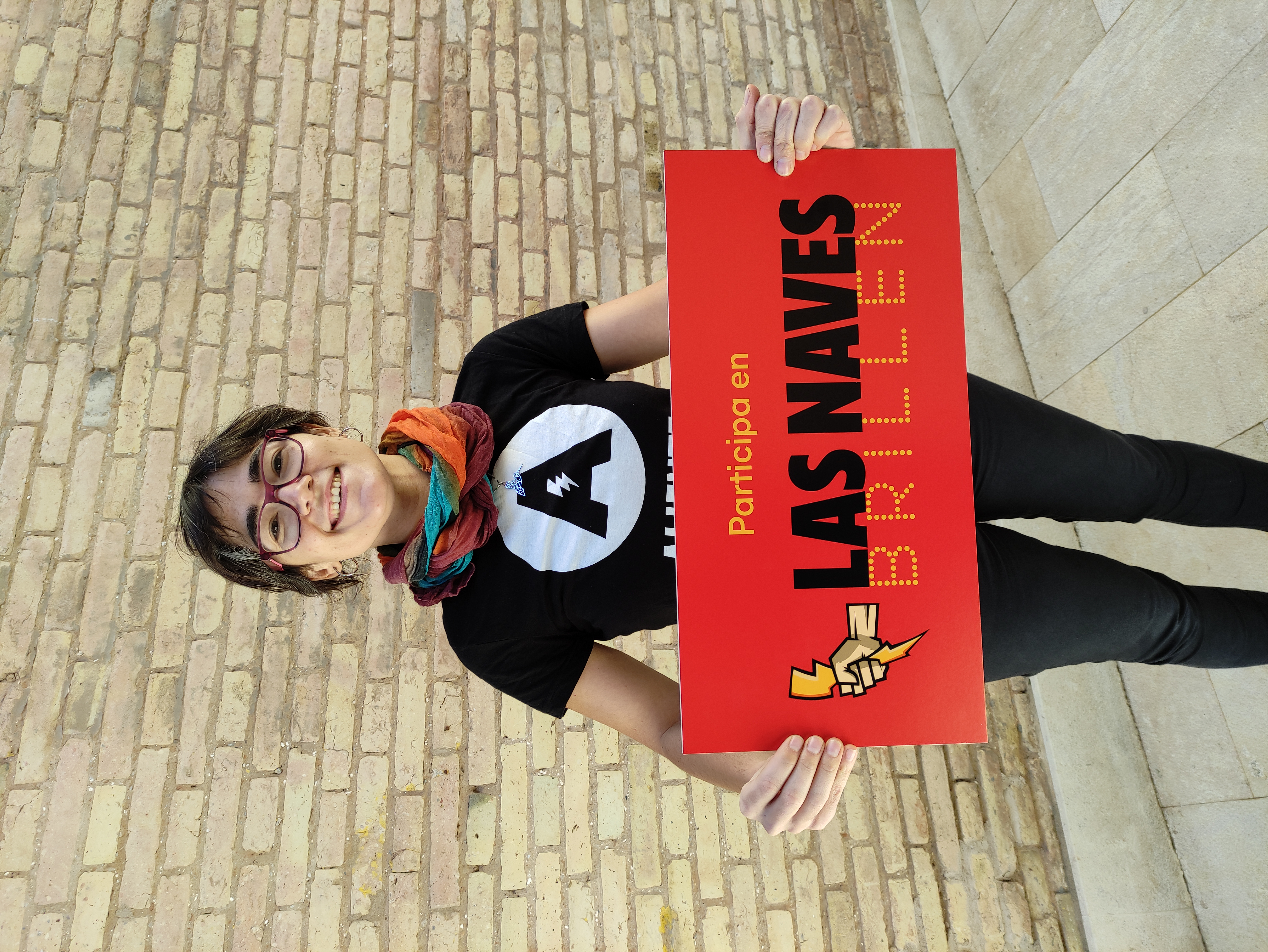 Fotografía de una chica sujetando un cartel con el logotipo de Las Naves Brillen