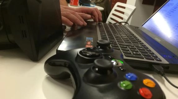 Fotografia de primer pla de les mans d'un gamer davant un ordinador i amb comandament de vdeojoc